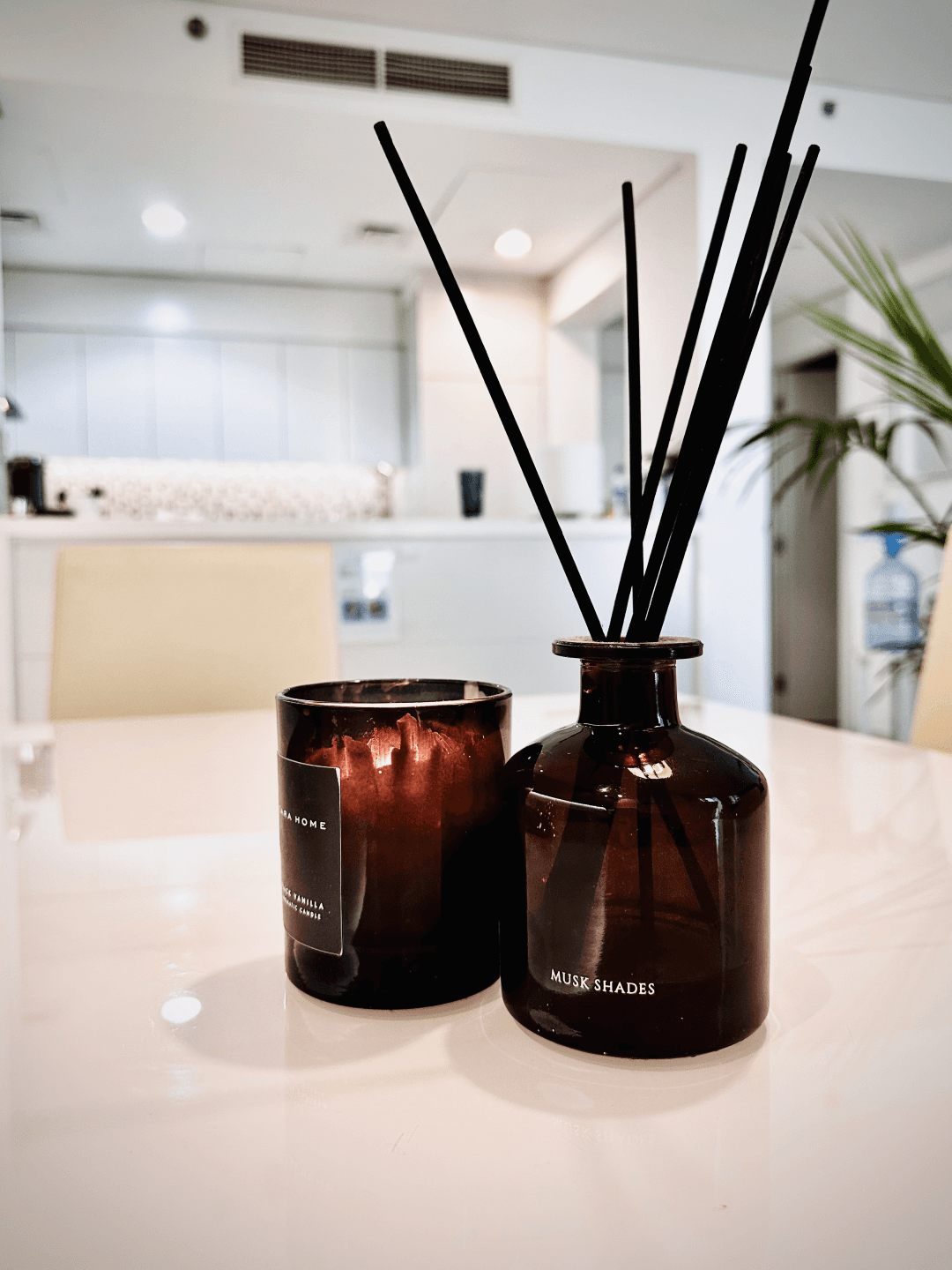 A photograph of a brown glass candle and an aroma diffuser placed on a white table in the living space at InterCube hostel in Dubai