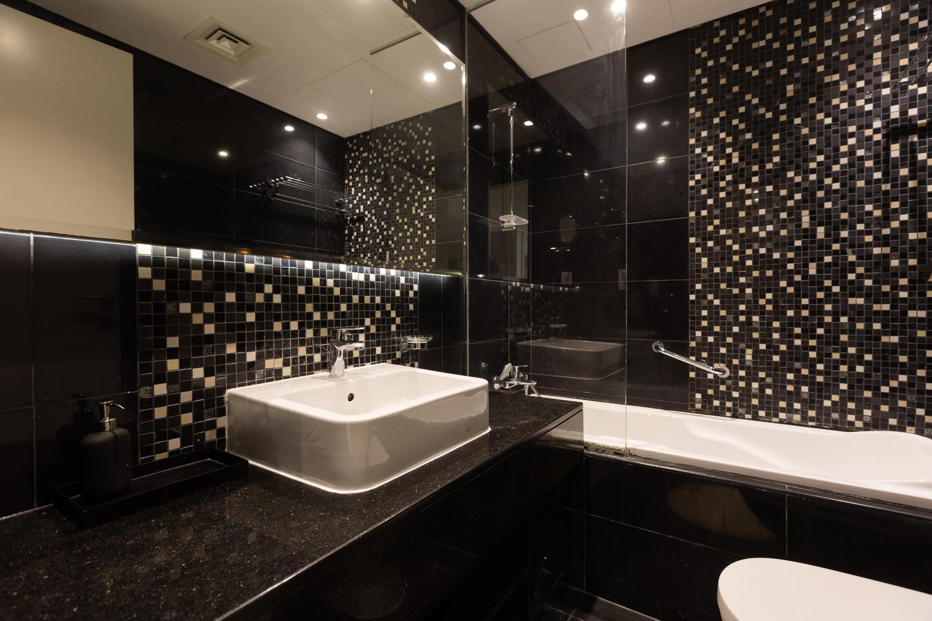 A photograph of the bathroom at InterCube hostel in Dubai, featuring a modern sink, a black tiled wall with a mosaic pattern, and a bathtub