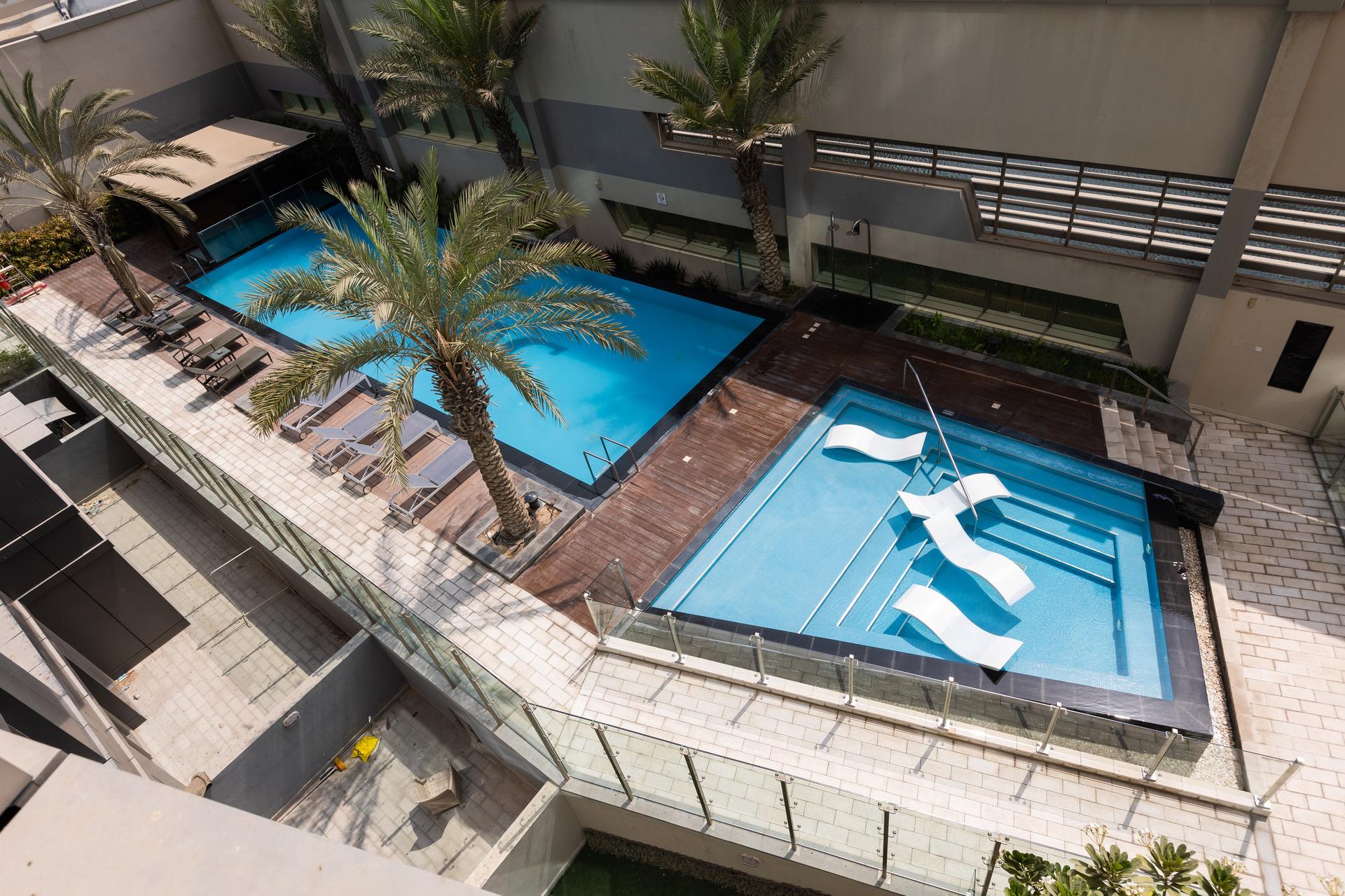 Photograph of the outdoor swimming pool area at InterCube hostel in Dubai, featuring two pools and lounge chairs surrounded by palm trees