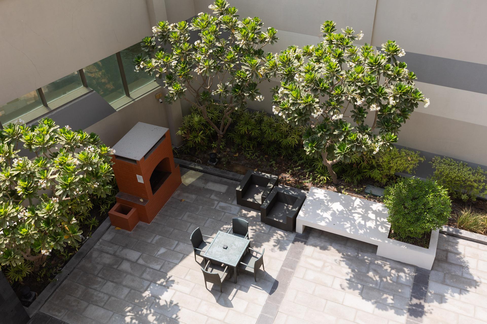 Photograph of the outdoor seating area at InterCube hostel in Dubai, featuring a table with chairs, lounge seating, and lush green plants