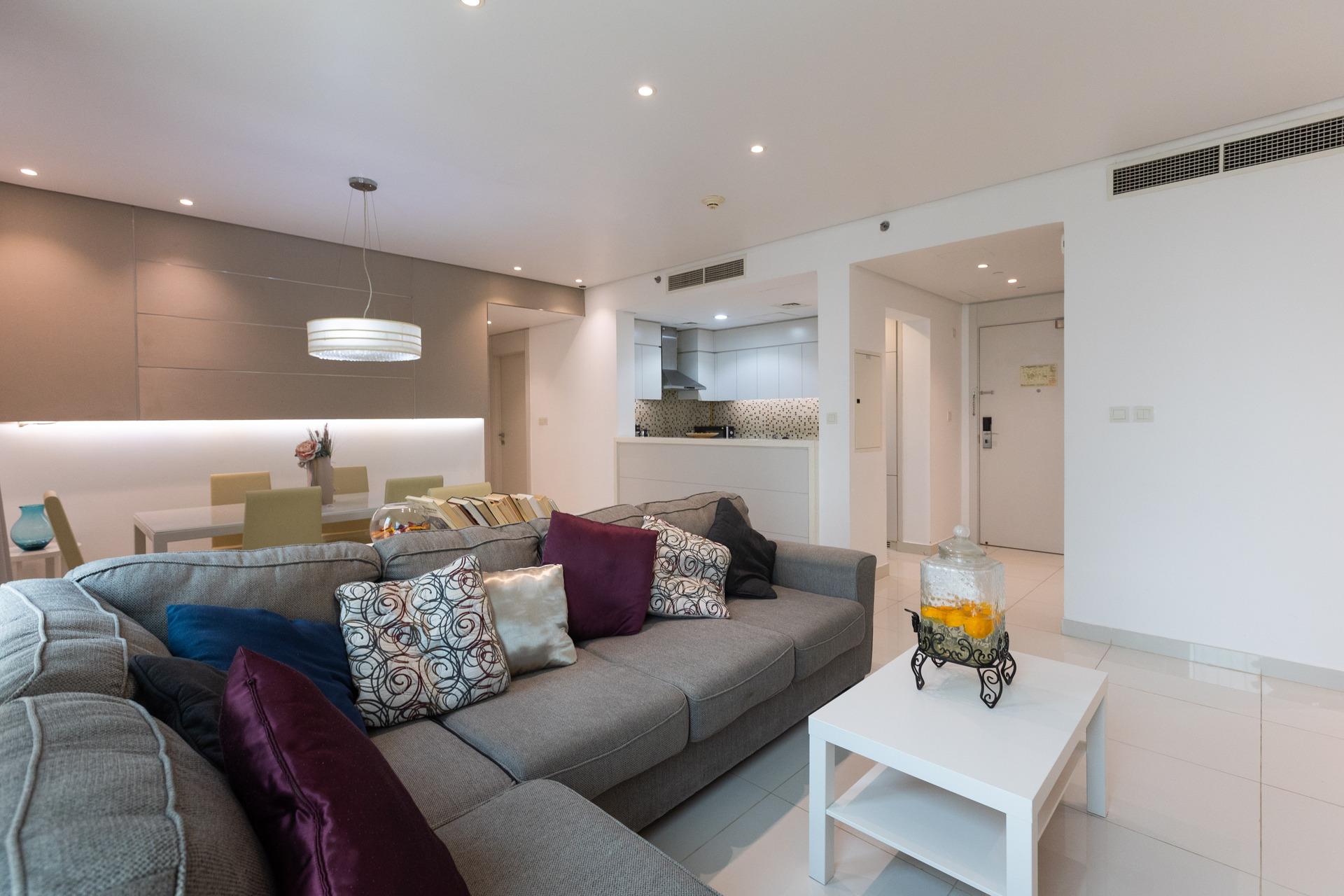 Photograph of a living room with a grey couch, a white coffee table, and a view of the kitchen at InterCube hostel in Dubai